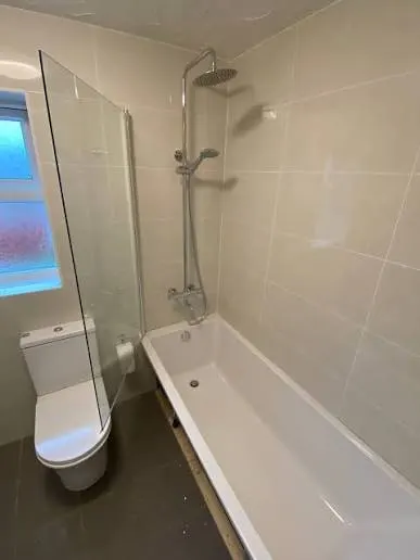 A renovated bath with a white tub, glass screen and beige tiling