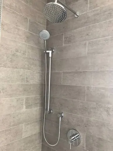 A chrome rainfall and hand shower set on grey woodgrain tile