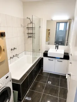 A compact bath refit with dark floor tile, tub screen and laundry