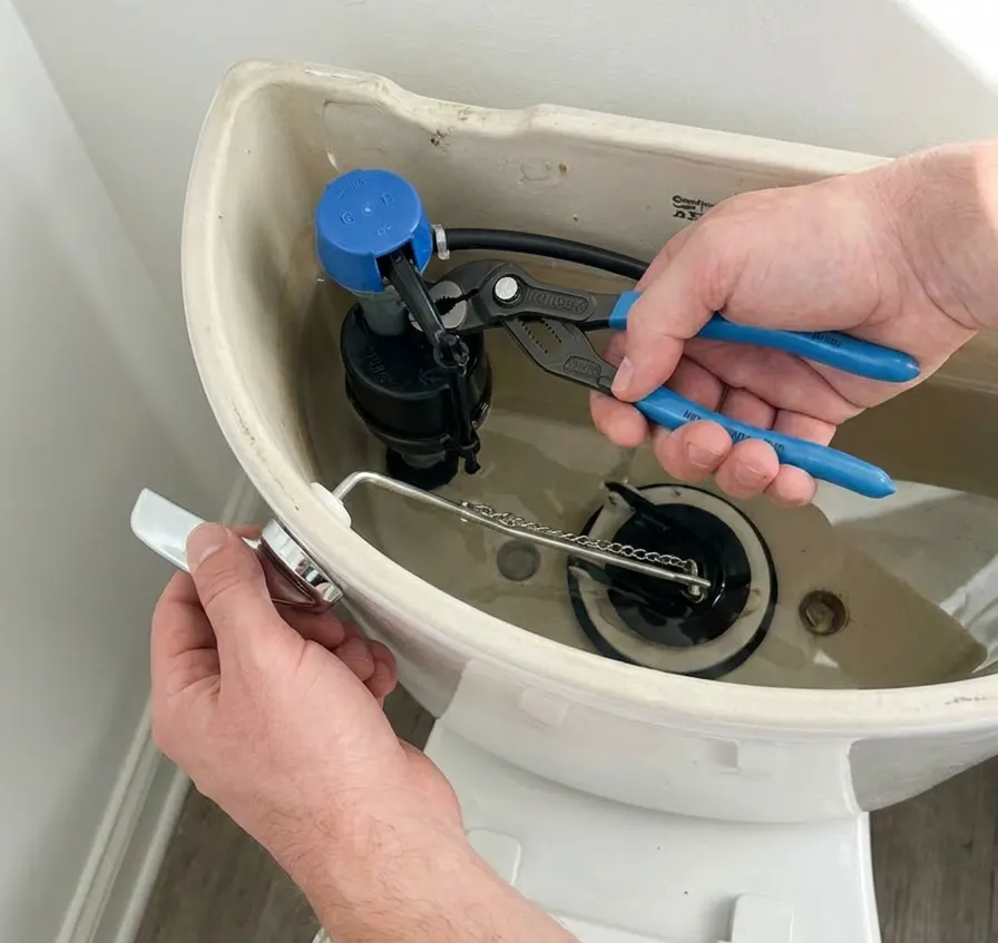 Hands repairing a toilet tank fill valve with a wrench