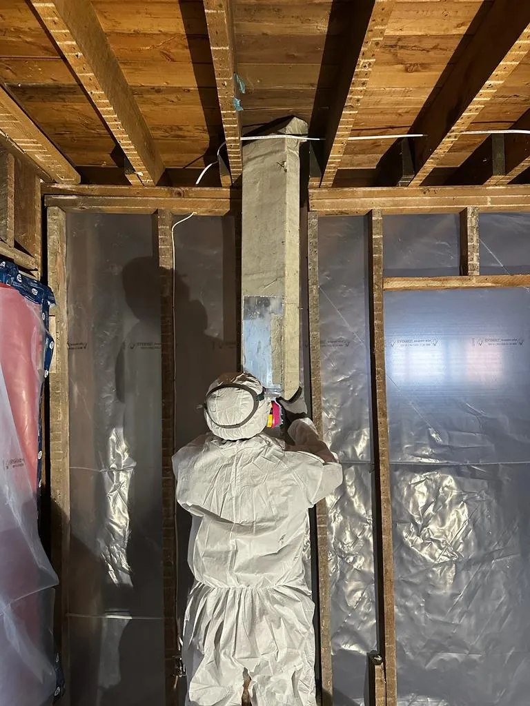 A craftsman in protective coveralls working on ductwork during a strip-out